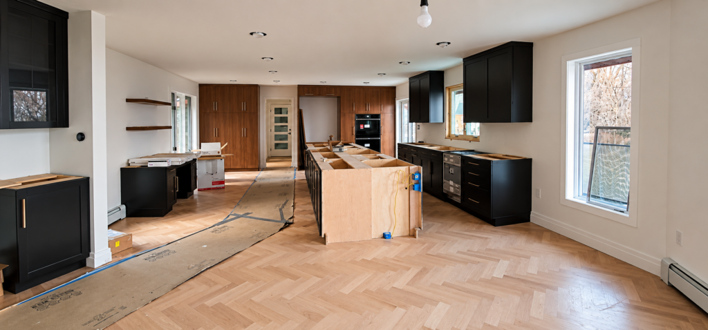Kitchen renovation in progress with new herringbone wood floors, partially installed cabinetry and an unfinished center island.