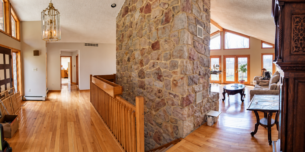 Original interior of our 1980s home before renovation, featuring a large stone fireplace, hardwood floors, wood trim, original stair railing and vaulted living room.